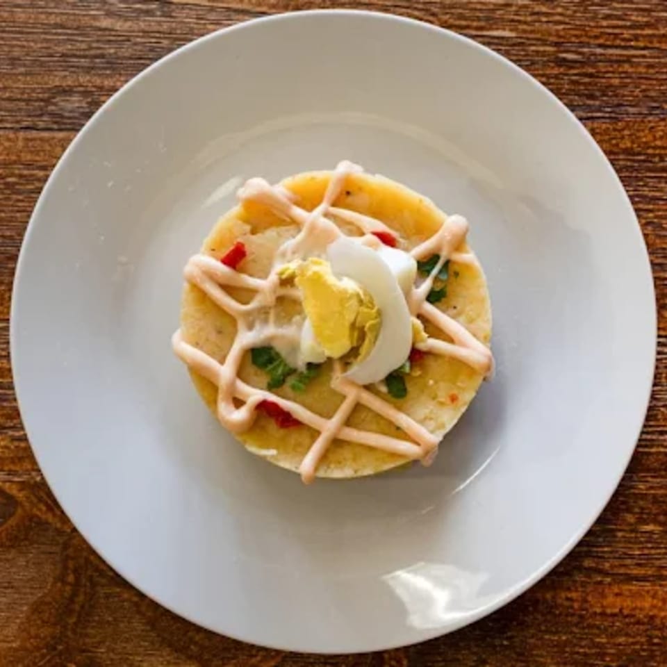Peruvian causa rellena, a layered potato dish, topped with a hard-boiled egg and creamy sauce.