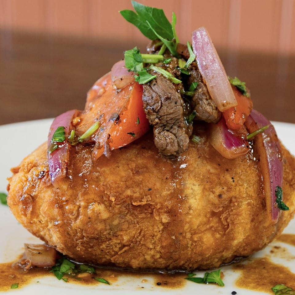 Peruvian papa rellena, a fried potato ball, topped with lomo saltado, red onions, and cilantro.