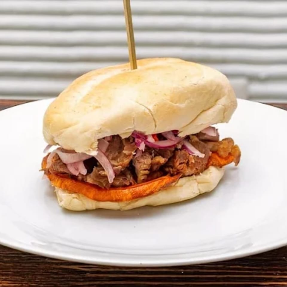 Peruvian sandwich with pork, sweet potato, and red onions on a white plate.
