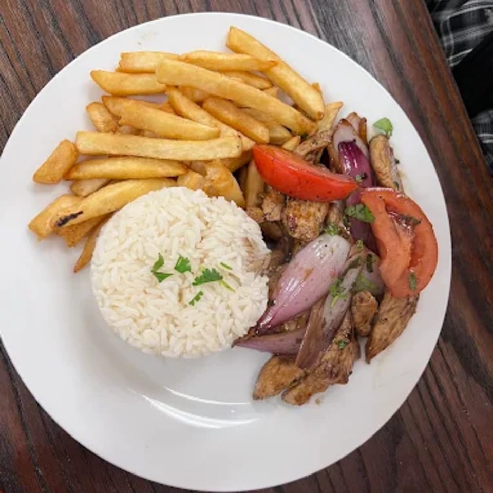 Peruvian Lomo Saltado with french fries, white rice, stir-fried beef, red onion, and tomatoes.