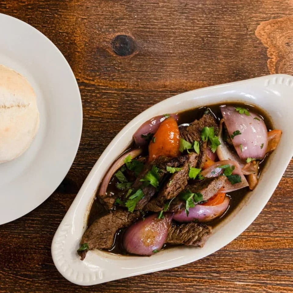 Peruvian Lomo Saltado, a stir-fry of beef, red onions, and tomatoes, served with a bread roll.